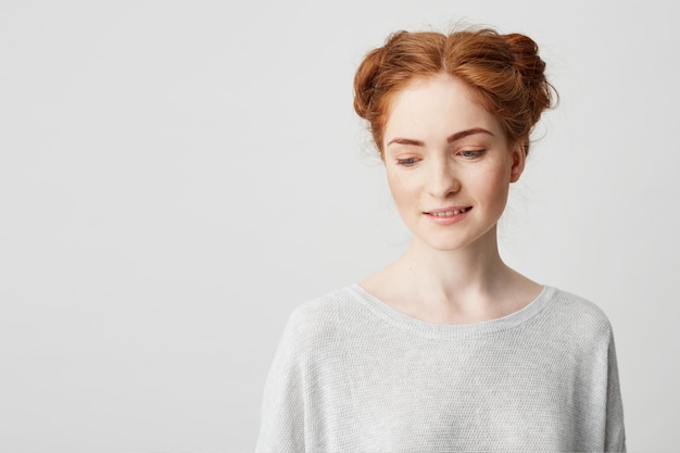 Portrait of shy young pretty redhead girl with buns looking down smiling .