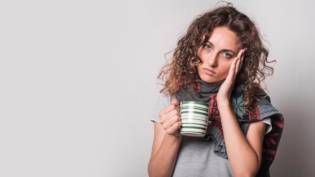 Portrait of sick woman holding coffee mug against gray background