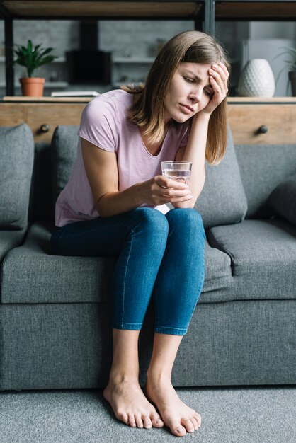 Portrait of a sick woman sitting on sofa with glass of water