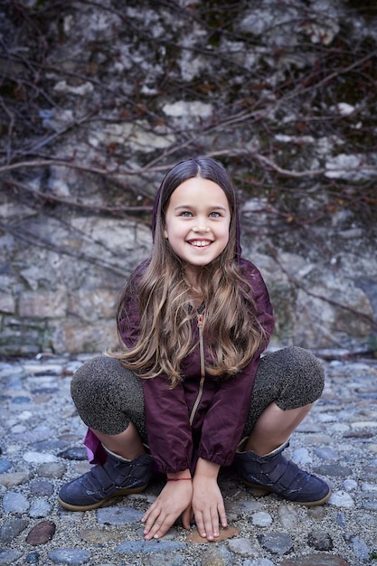 Портрет сидящей девушки-подростка на скалах, одетой в толстовку с капюшоном.