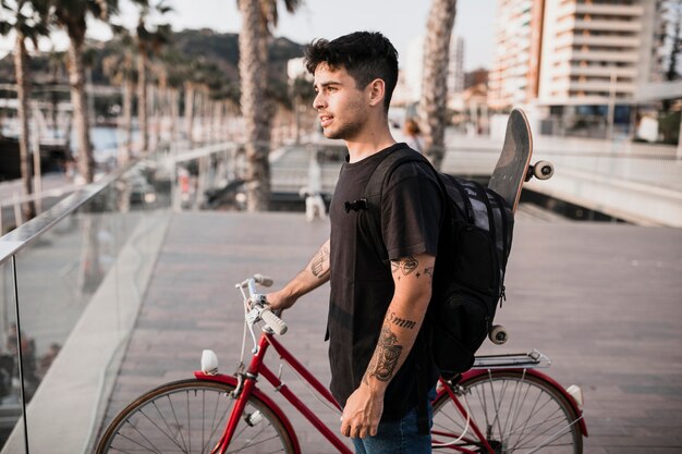 Portrait of skateboarder standing with bicycle