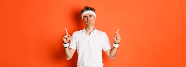 Portrait of skeptical adult sportsman in headband and tshirt complaining and pointing fingers up loo