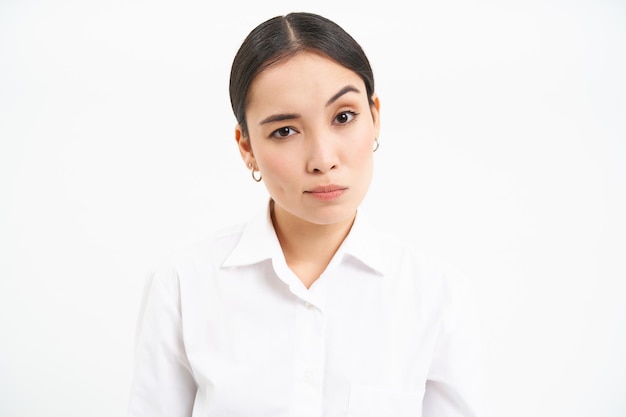 Free photo portrait of skeptical asian woman looks unamused and serious at camera stands isolated on white back