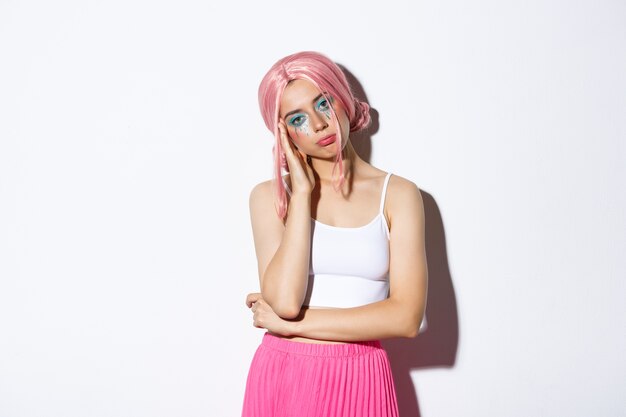 Portrait of sleepy cute girl looking bored at halloween party, wearing pink wig and skirt, standing unamused.