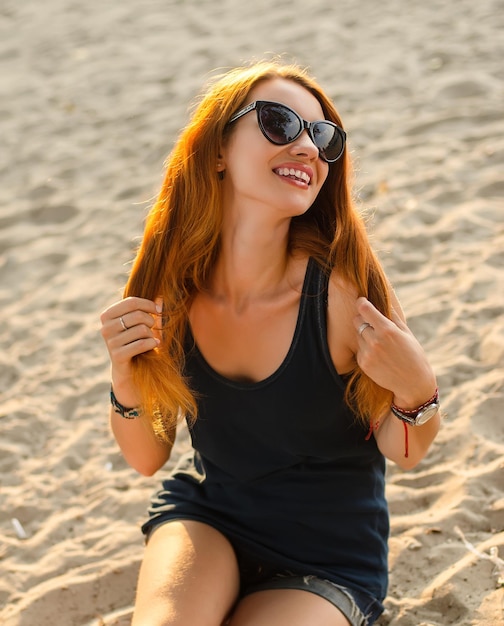 Portrait of a slim redhead woman sits on a beach.