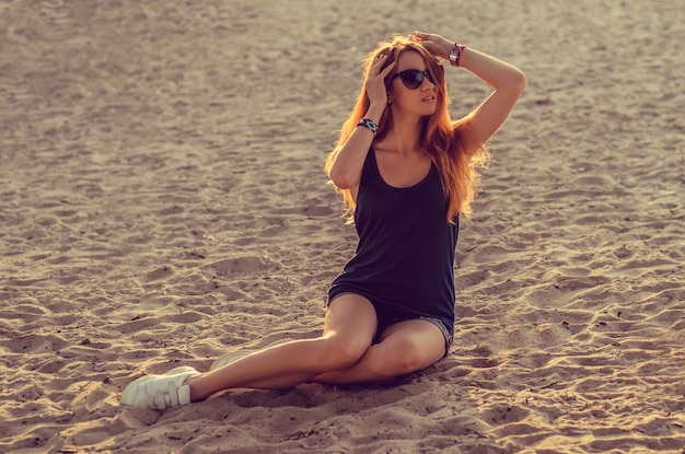 Portrait of a slim redhead woman sits on a beach.