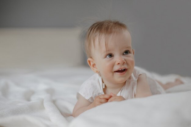 미소의 초상화는 흰색 침대 시트에 누워 큰 눈을 가진 작은 귀여운 아기 소녀를 궁금해했습니다.