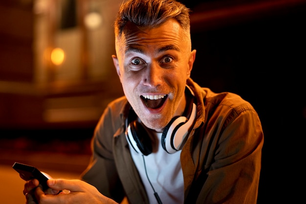 Portrait of smiley man in the city at night with headphones and smartphone