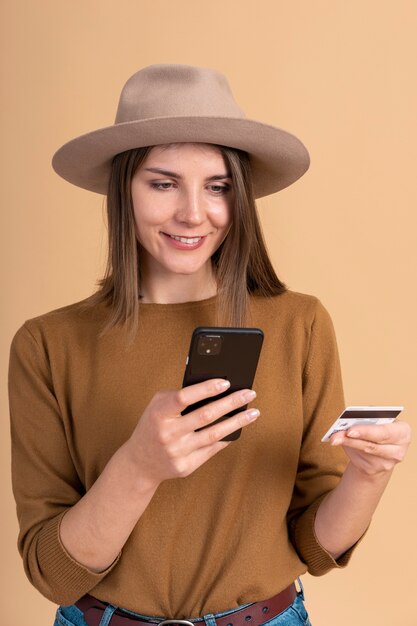 Portrait of smiley woman with hat booking travel tickets with smartphone and credit card