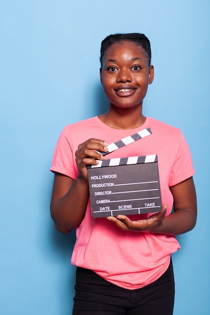 Portrait of smiling african american young woman holding filmography clapboard