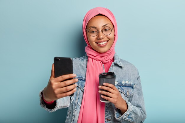 笑顔のアラビアの女の子の肖像画が携帯電話で自分撮りをします