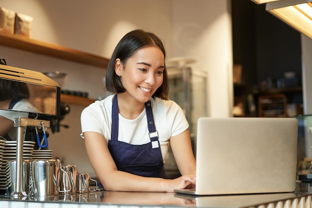 com で注文を処理するラップトップに取り組んでいる笑顔のアジアのバリスタ カフェ オーナー起業家の肖像画