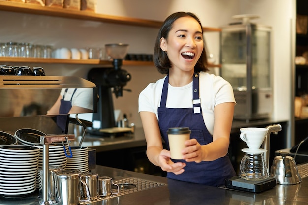 Free photo portrait of smiling asian girl barista giving out order in cafe inviting guest to pick up takeaway o