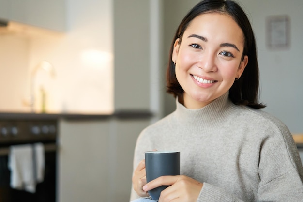 따뜻한 차를 마시고 집에서 아늑해지는 커피 한 잔과 함께 웃고 있는 아시아 소녀의 초상화
