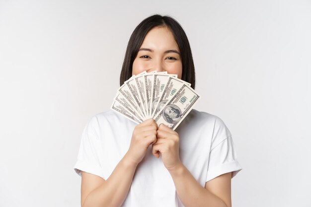 白い背景の上に立っているマイクロクレジット金融と現金のドルのお金の概念を保持している笑顔のアジアの女性の肖像画