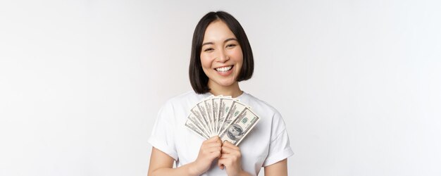 흰색 배경 위에 서 있는 소액 신용 금융과 현금의 달러화 개념을 들고 웃고 있는 아시아 여성의 초상화