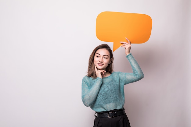 Portrait of a smiling asian woman holding empty orange speech bubble isolated over gray wall