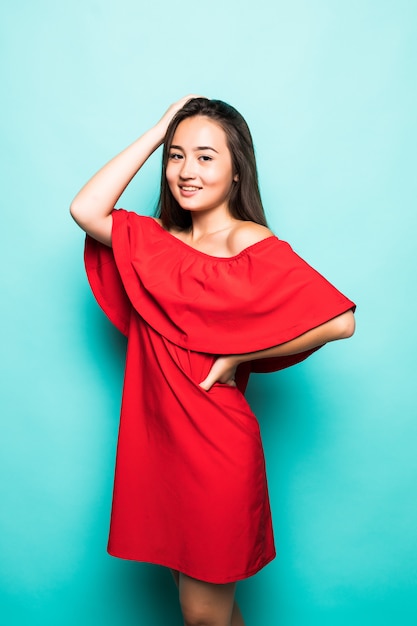 빨간 드레스 서 웃는 아시아 여자의 초상화 청록색 배경 위에 절연 카메라를 찾고