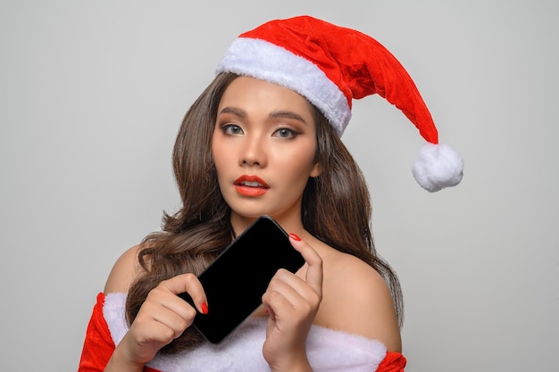 Portrait of smiling asian woman in red santa claus costume posing with smartphone