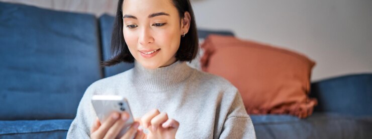 無料Photo 家に座る笑顔のアジア人女性のポートレートは、スマートフォンのアプリを使用して、誰かに配達メッセージを注文します