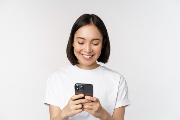 白い背景の上のTシャツに立っている携帯電話チャットテキストメッセージメッセージを使用して笑顔のアジアの女性の肖像画コピースペース