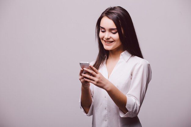 흰색 배경 위에 절연 서있는 동안 휴대 전화에 웃는 매력적인 여자 문자 메시지의 초상화