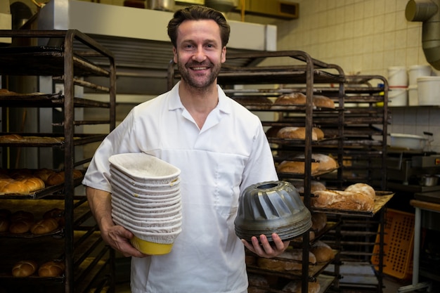 Portrait of smiling baker holding mould and stack of tray