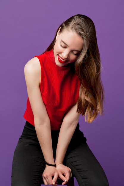 Portrait of smiling beautiful brunette girl with long wavy hair dressed red t-shirt smiling with shy view against of purple wall. Isolated. Summer mood. Sensitive portrait