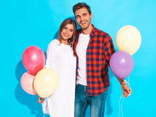 Portrait of Smiling Beautiful Girl and her Handsome Boyfriend holding bunch of colorful balloons and laughing. Happy Birthday