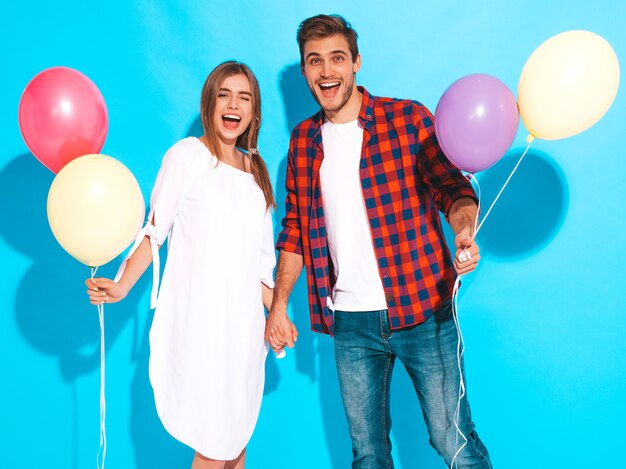 Portrait of Smiling Beautiful Girl and her Handsome Boyfriend holding bunch of colorful balloons and laughing. Happy Birthday