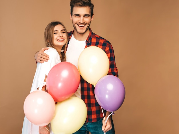 Portrait of Smiling Beautiful Girl and her Handsome Boyfriend holding bunch of colorful balloons and laughing. Happy couple in love. Happy Birthday