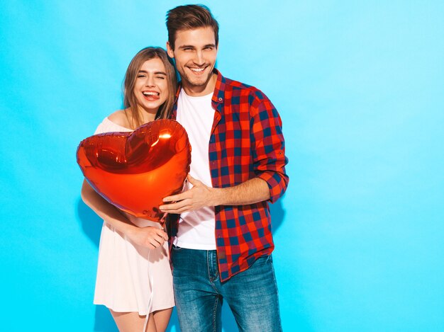 Portrait of Smiling Beautiful Girl and her Handsome Boyfriend holding heart shaped balloons and laughing. Happy couple in love. Happy Valentine's Day. Posing