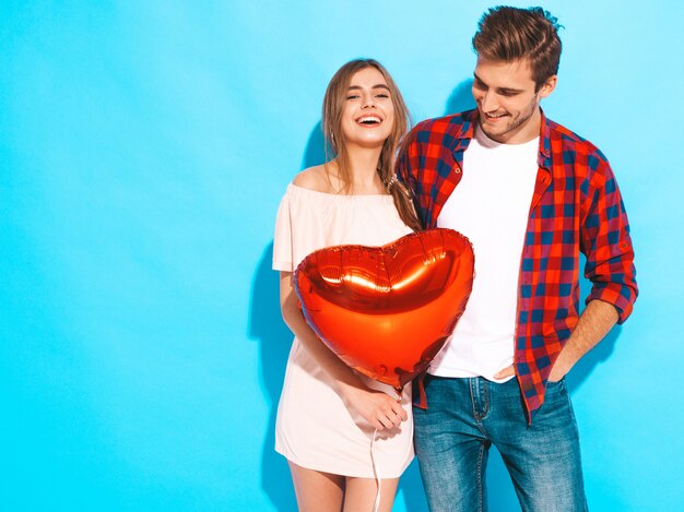 Portrait of Smiling Beautiful Girl and her Handsome Boyfriend holding heart shaped balloons and laughing. Happy couple in love. Happy Valentine's Day. Posing