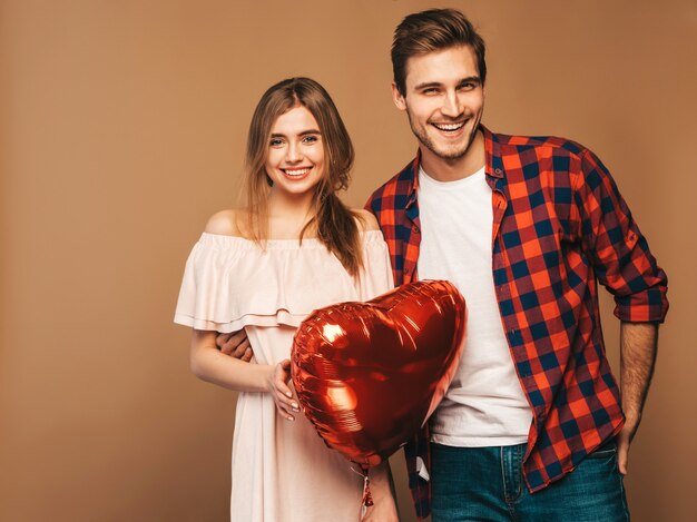 Portrait of Smiling Beautiful Girl and her Handsome Boyfriend holding heart shaped balloons and laughing. Happy couple in love. Happy Valentine's Day. 