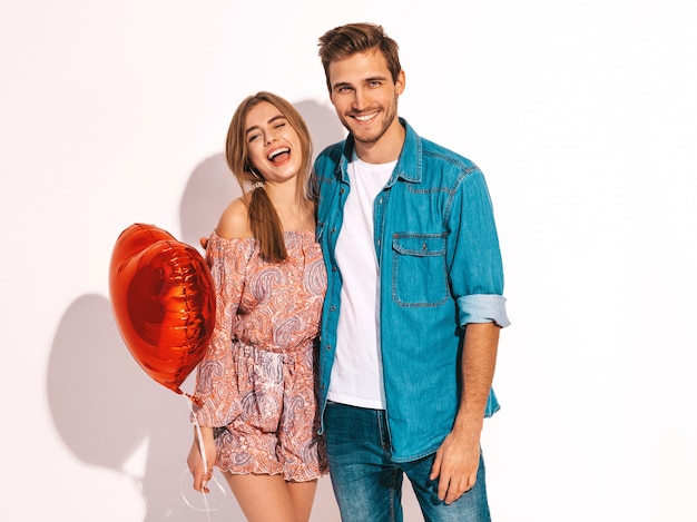 Portrait of Smiling Beautiful Girl and her Handsome Boyfriend holding heart shaped balloons and laughing. Happy couple in love. Happy Valentine's Day. 