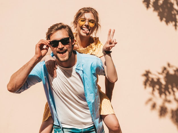 Portrait of smiling beautiful girl and her handsome boyfriend. Woman in casual summer dress and man in jeans. Happy cheerful family. Female having fun in the street near wall