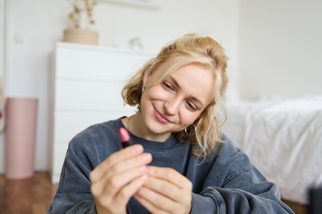 彼女の部屋で笑顔の美しい女性の肖像画が座って,リップスティックを示し,お気に入りを推奨しています