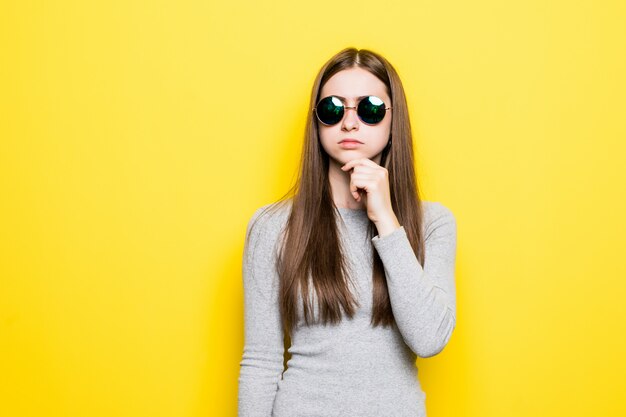 Portrait of smiling beautiful woman in sunglasses and dress against of yellow wall