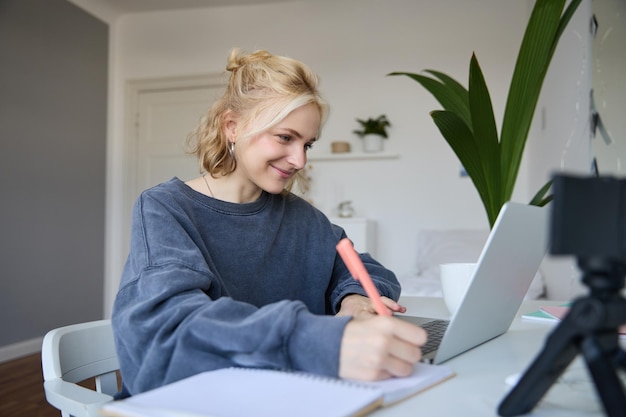 Free photo portrait of smiling blond woman writing in notebook making notes recording content for social medial