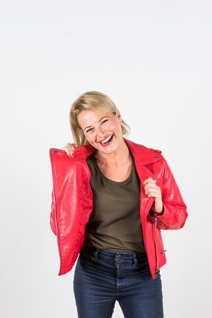 Portrait of smiling blonde mature woman in red jacket standing against white background