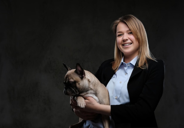 Portrait of a smiling blonde woman breeder holds her cute pug. Isolated on a dark textured background.