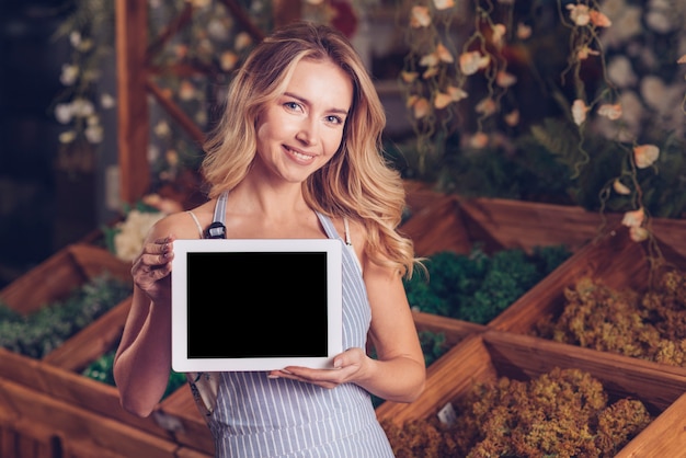 Free photo portrait of a smiling blonde young female florist showing digital tablet with black screen display