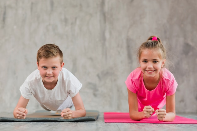 Portrait of a smiling boy and girl doing fitness exercise in front of concrete wall