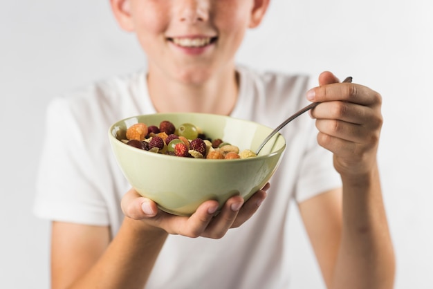 Portrait of smiling boy holding bowl of fruit salad against white background
