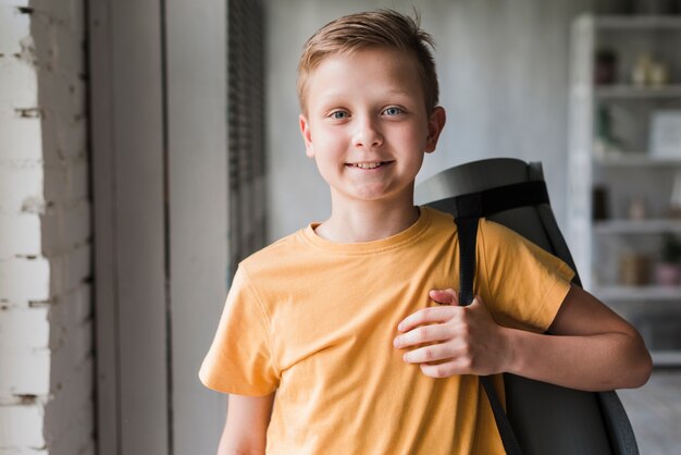 Portrait of a smiling boy holding exercise mat on his shoulder