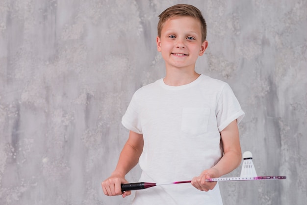 Portrait of a smiling boy holding racket and shuttlecock looking at camera