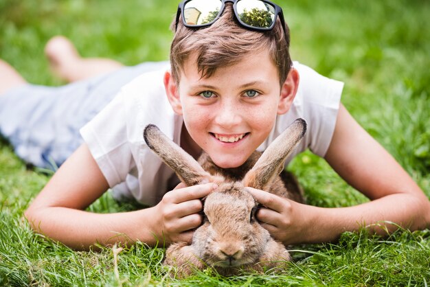 Portrait of smiling boy lying over rabbit on green grass in the park