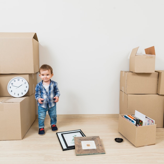 Free photo portrait of a smiling boy standing near the cardboard boxes at his new house