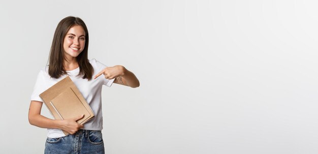 Ritratto di ragazza bruna sorridente che punta il dito contro il concetto di notebook di corsi o studio