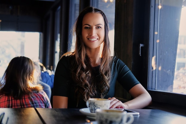 Portrait of smiling brunette woman drinks morning coffee in a cafe.